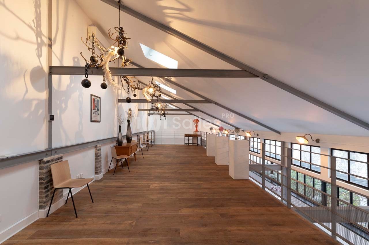 Intérieur d'un loft avec mezzanine, parquet en bois, mobilier minimaliste et grandes fenêtres laissant entrer la lumière.