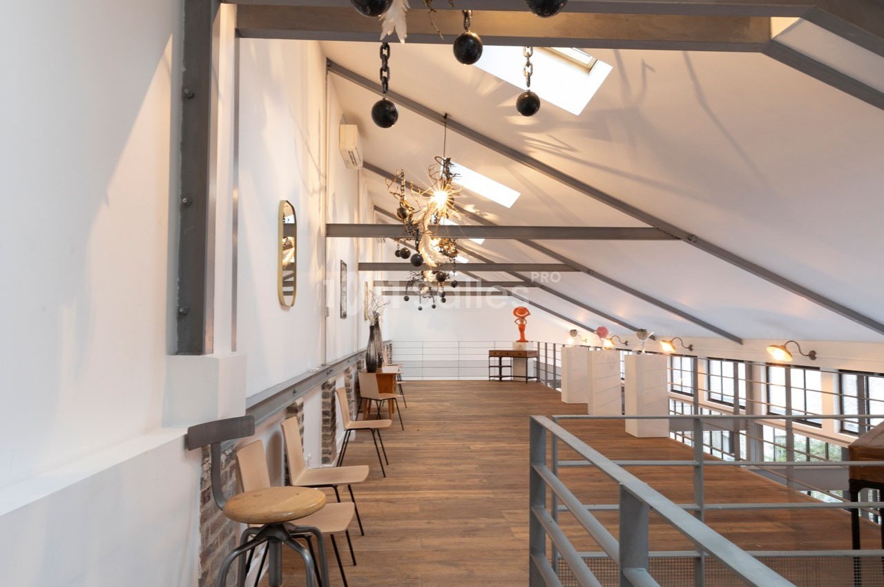 Intérieur d'un espace mansardé lumineux avec parquet, chaises en bois, poutres apparentes et décorations suspendues.