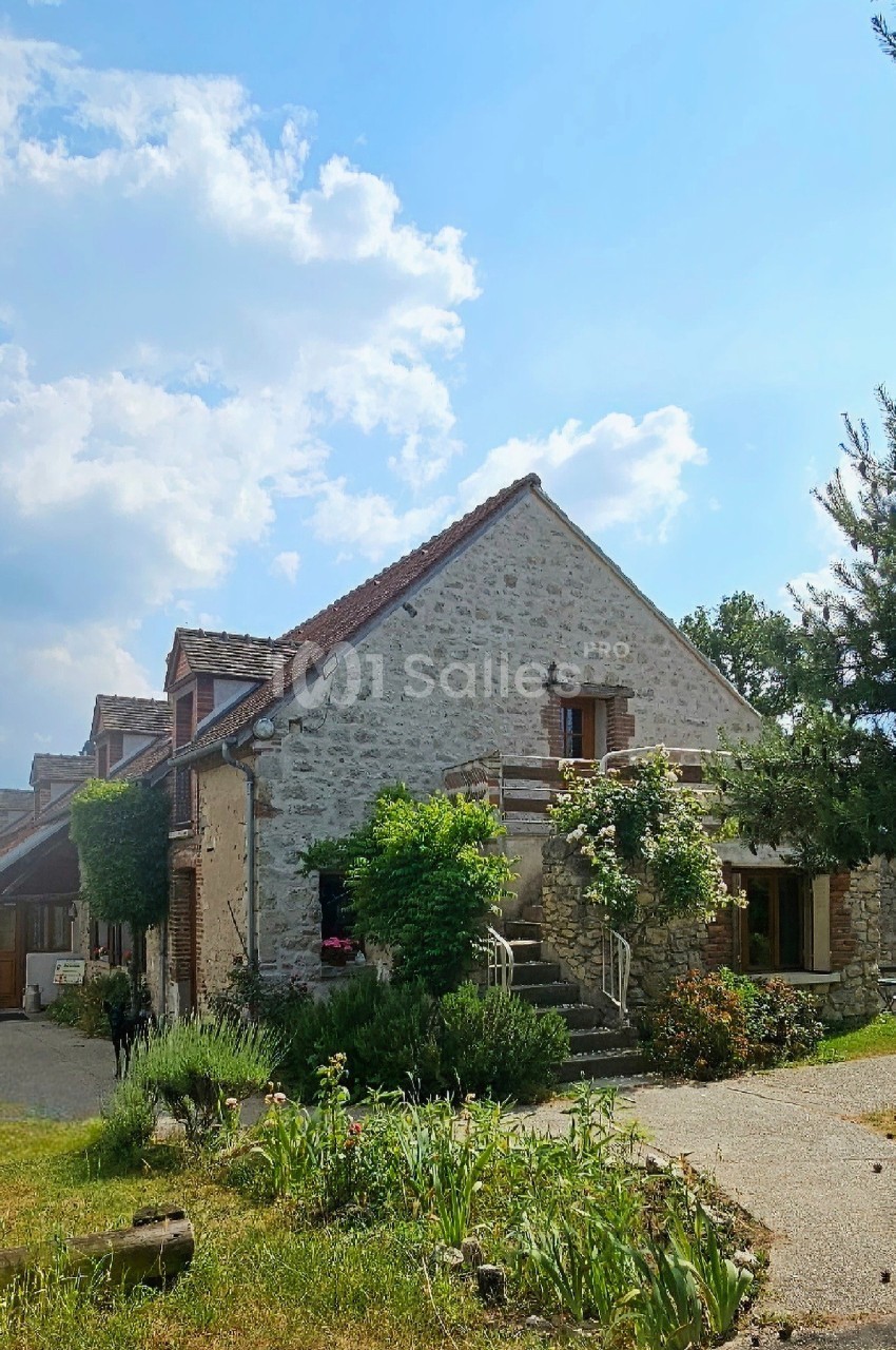 Maison en pierre entourée de verdure, avec un ciel bleu et quelques nuages en arrière-plan.