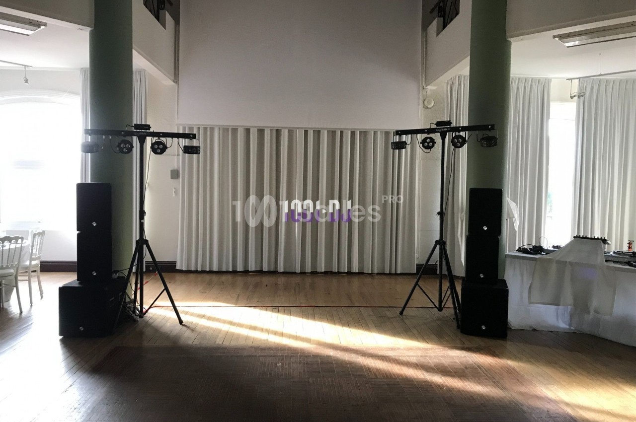 Installation de matériel de sonorisation et d'éclairage dans une salle lumineuse avec rideaux blancs.