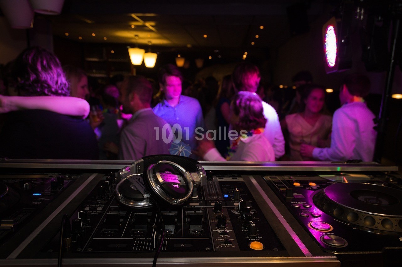 Console de DJ avec casque au premier plan, devant une foule dansante dans une ambiance lumineuse tamisée.