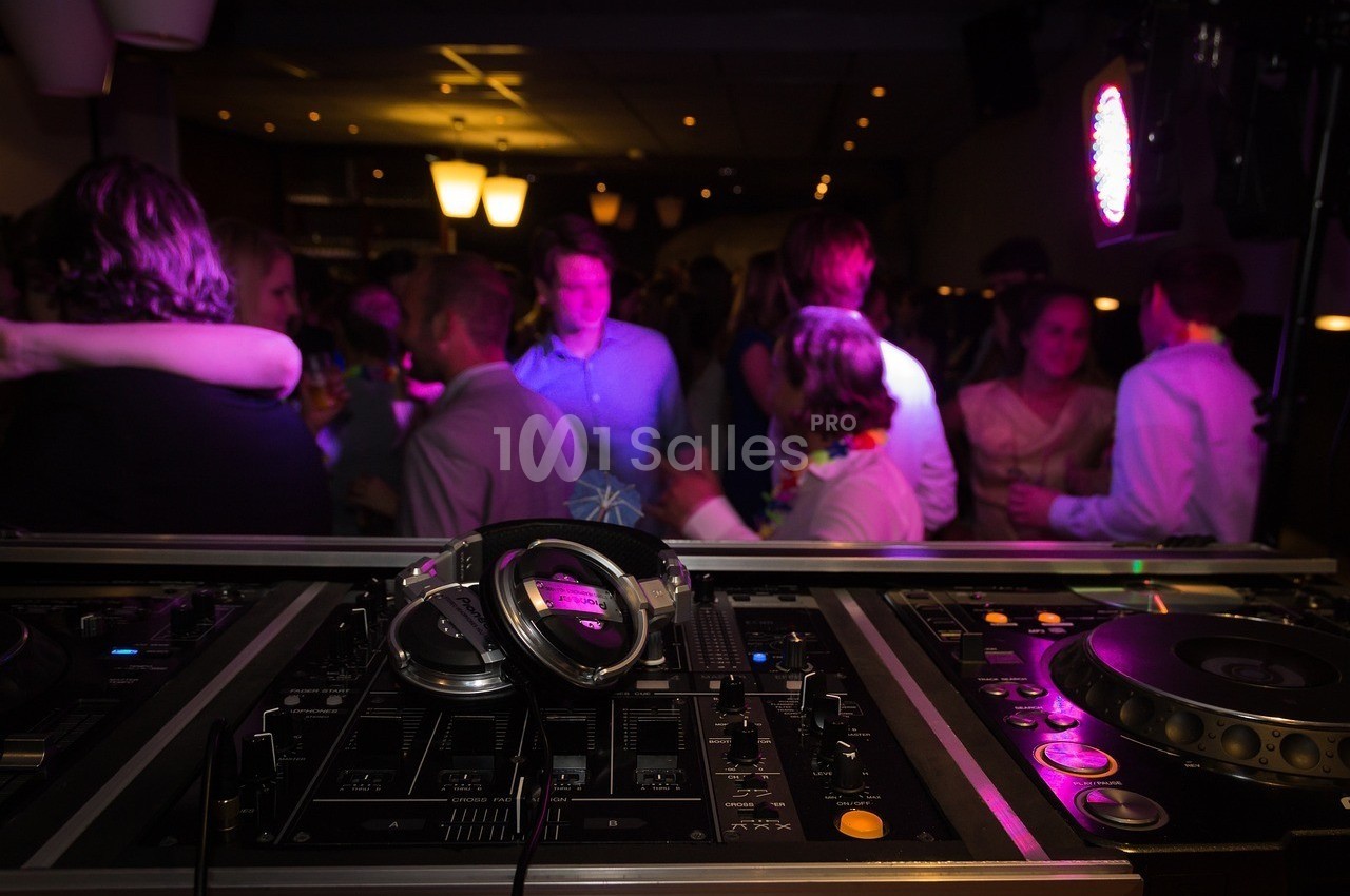 Vue d'une table de mixage avec des casques audio au premier plan, et une foule dansante en arrière-plan.
