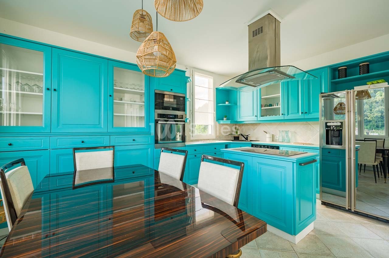 Cuisine moderne avec armoires turquoise, table en bois foncé, électroménagers intégrés et suspensions en osier.