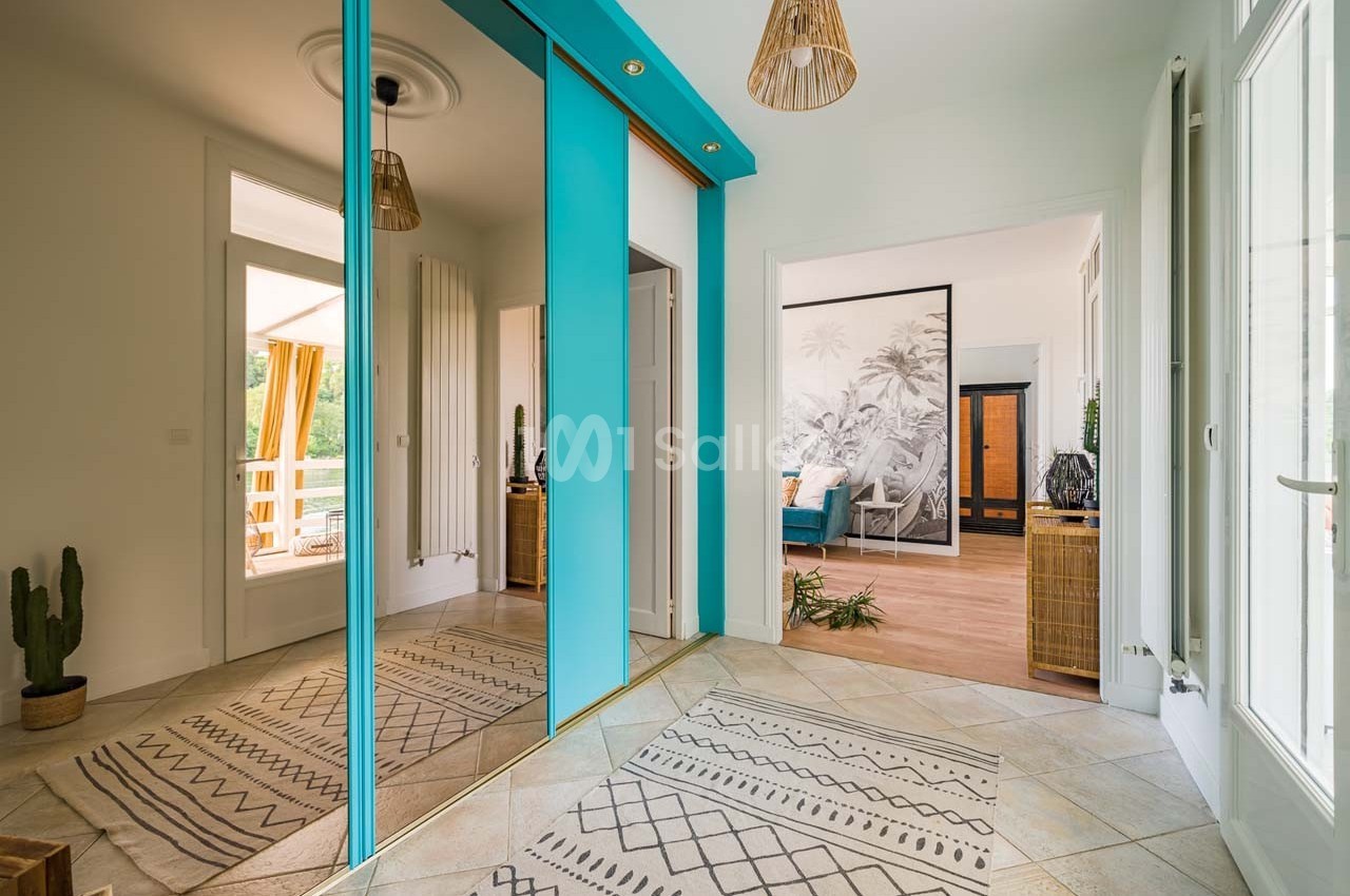 Entrée lumineuse avec placards à portes miroir, tapis à motifs géométriques et vue sur un salon et une terrasse.