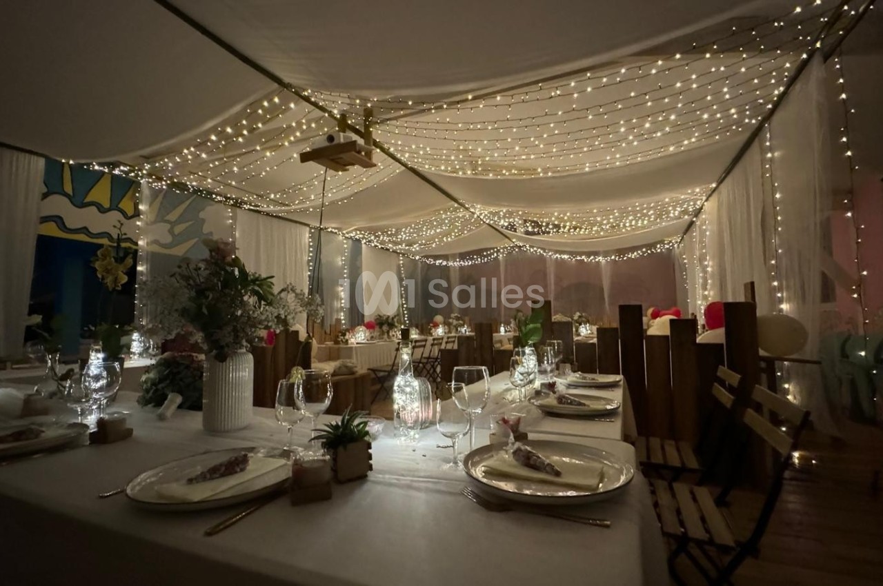 Salle de réception décorée avec des guirlandes lumineuses suspendues, tables dressées et ambiance chaleureuse.