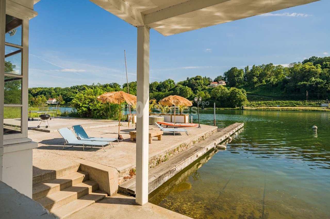 Terrasse au bord d’un lac avec transats, parasols en paille et végétation verdoyante en arrière-plan.