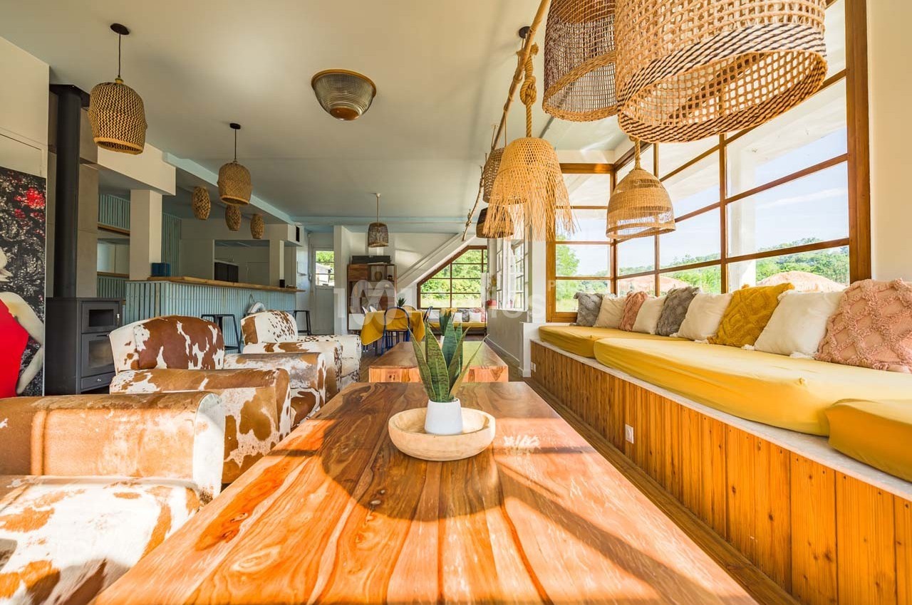 Salle lumineuse avec table en bois, fauteuils à motifs, banquette jaune et suspensions en osier.