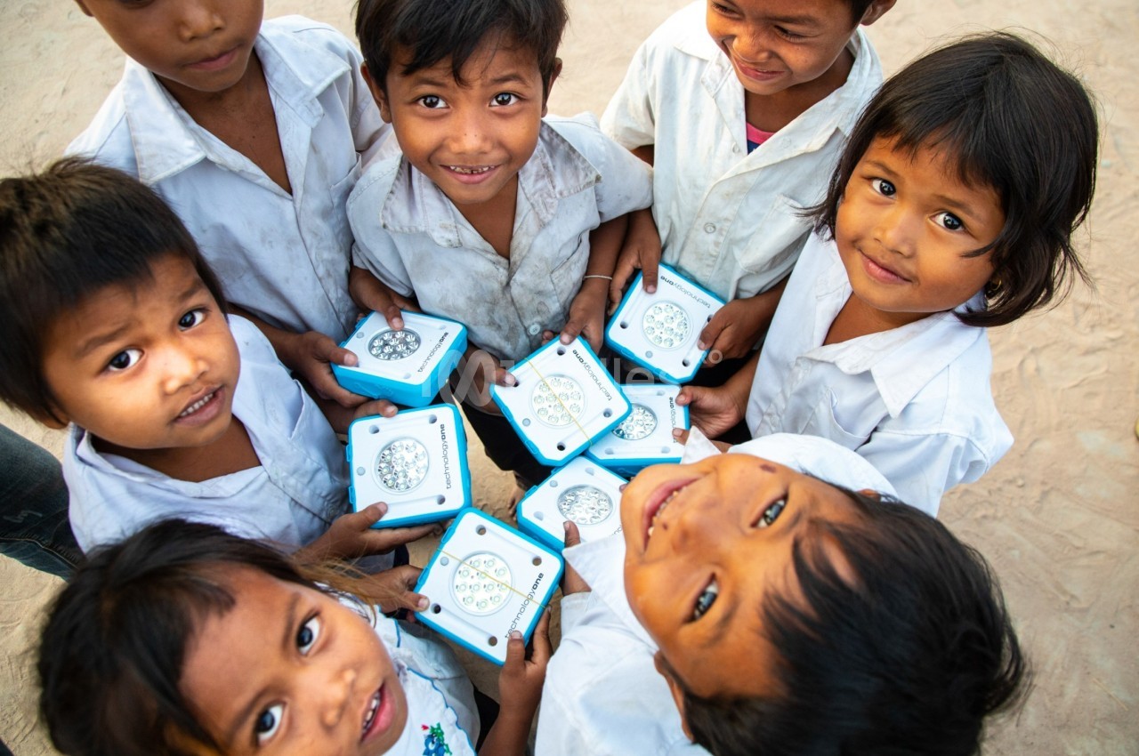Des enfants souriants en uniforme scolaire tiennent des lampes solaires bleues dans un environnement extérieur.