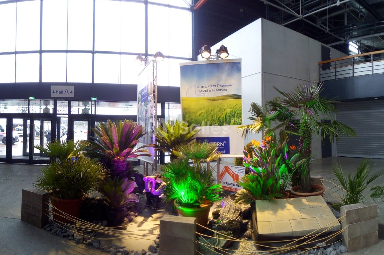 Exposition de plantes tropicales en pots avec éclairage coloré, située dans un hall à grande baie vitrée.