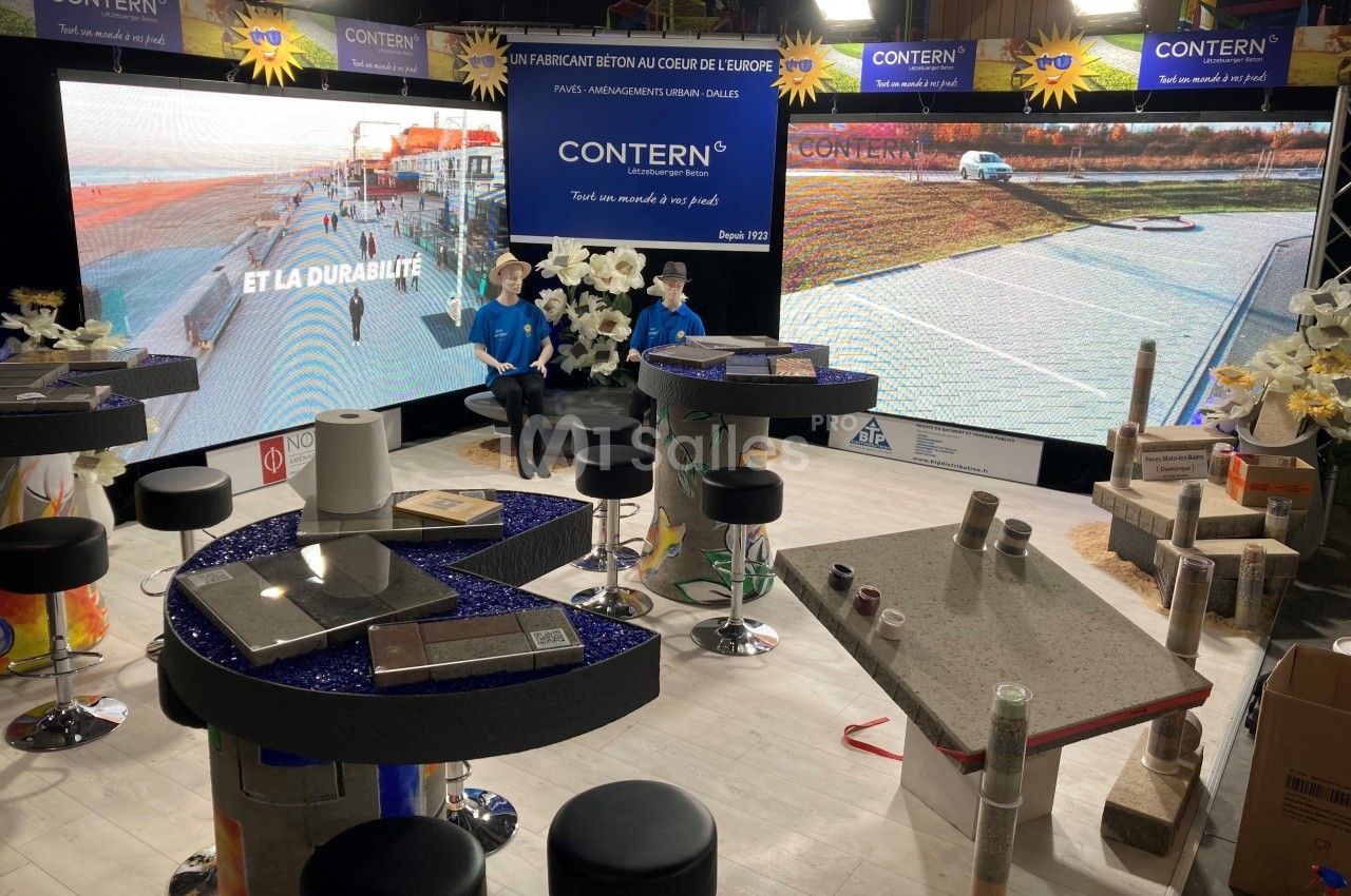 Stand d'exposition présentant des produits en béton, avec écrans, échantillons et décorations sur des tables.