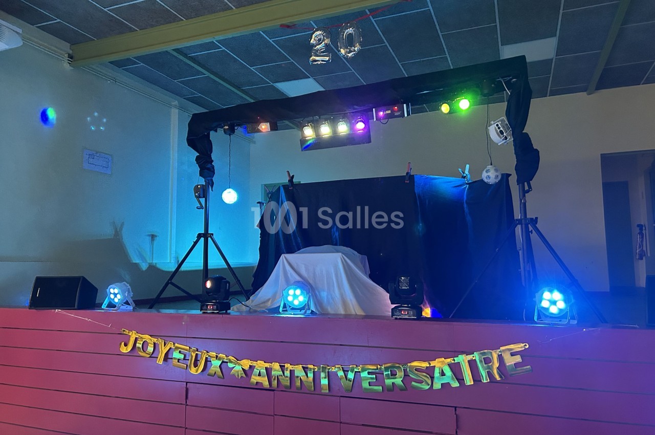 Scène décorée pour un anniversaire avec guirlande ’Joyeux Anniversaire’ et éclairages colorés suspendus.