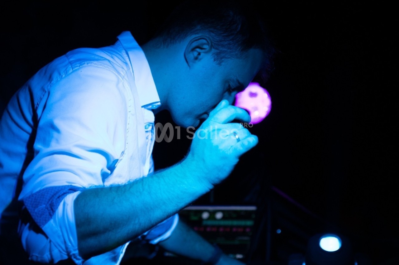 Homme en chemise blanche concentré, éclairé par une lumière bleue, devant un équipement électronique dans un environnement…