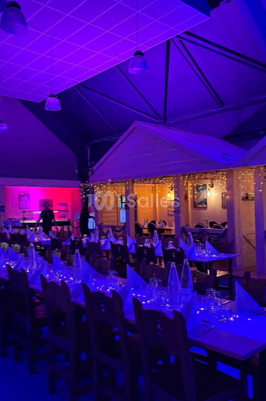 Salle de réception décorée avec des guirlandes lumineuses, tables dressées et éclairage tamisé bleu et rose.