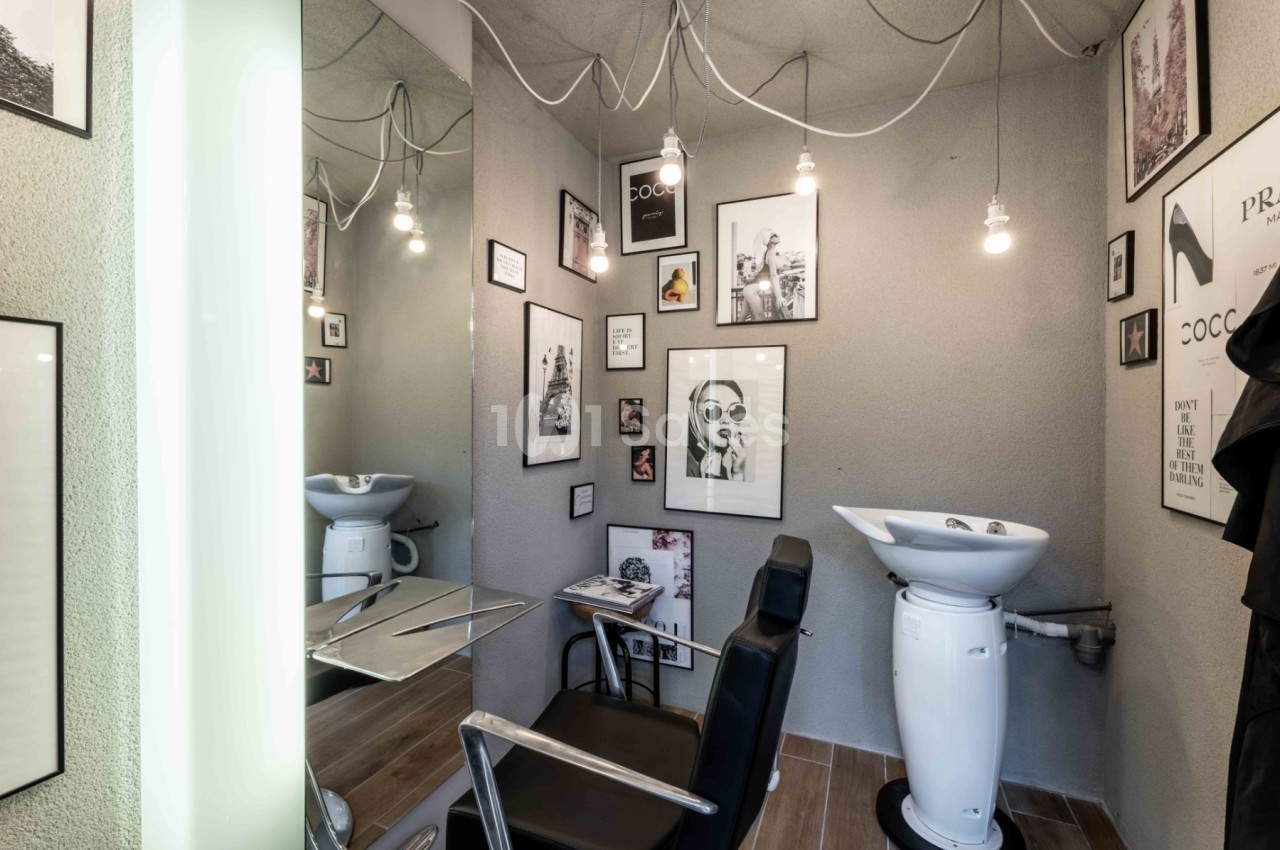 Coin de salon de coiffure moderne avec un fauteuil, un lavabo blanc et des cadres décoratifs accrochés aux murs.
