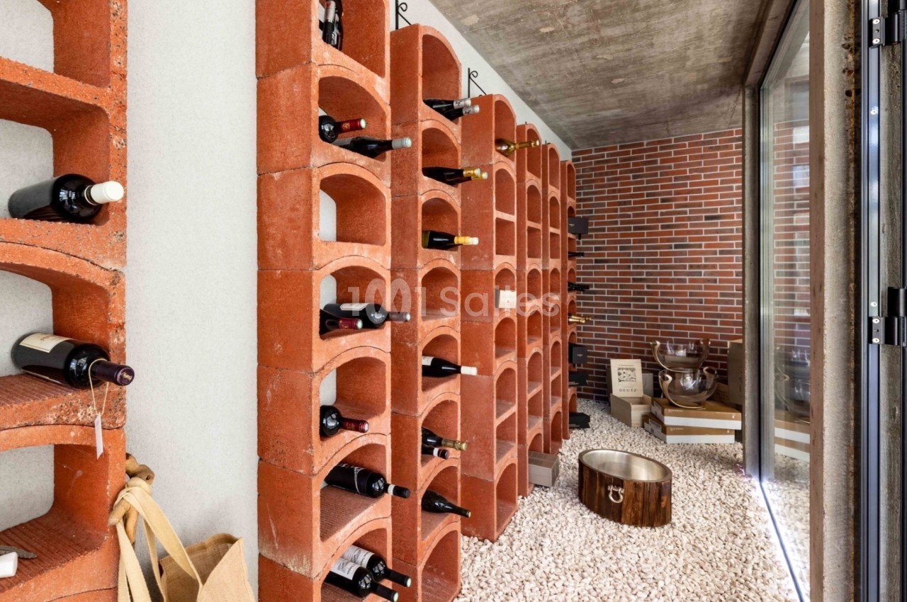 Cave à vin avec étagères en briques rouges, bouteilles rangées et sol recouvert de gravier blanc.