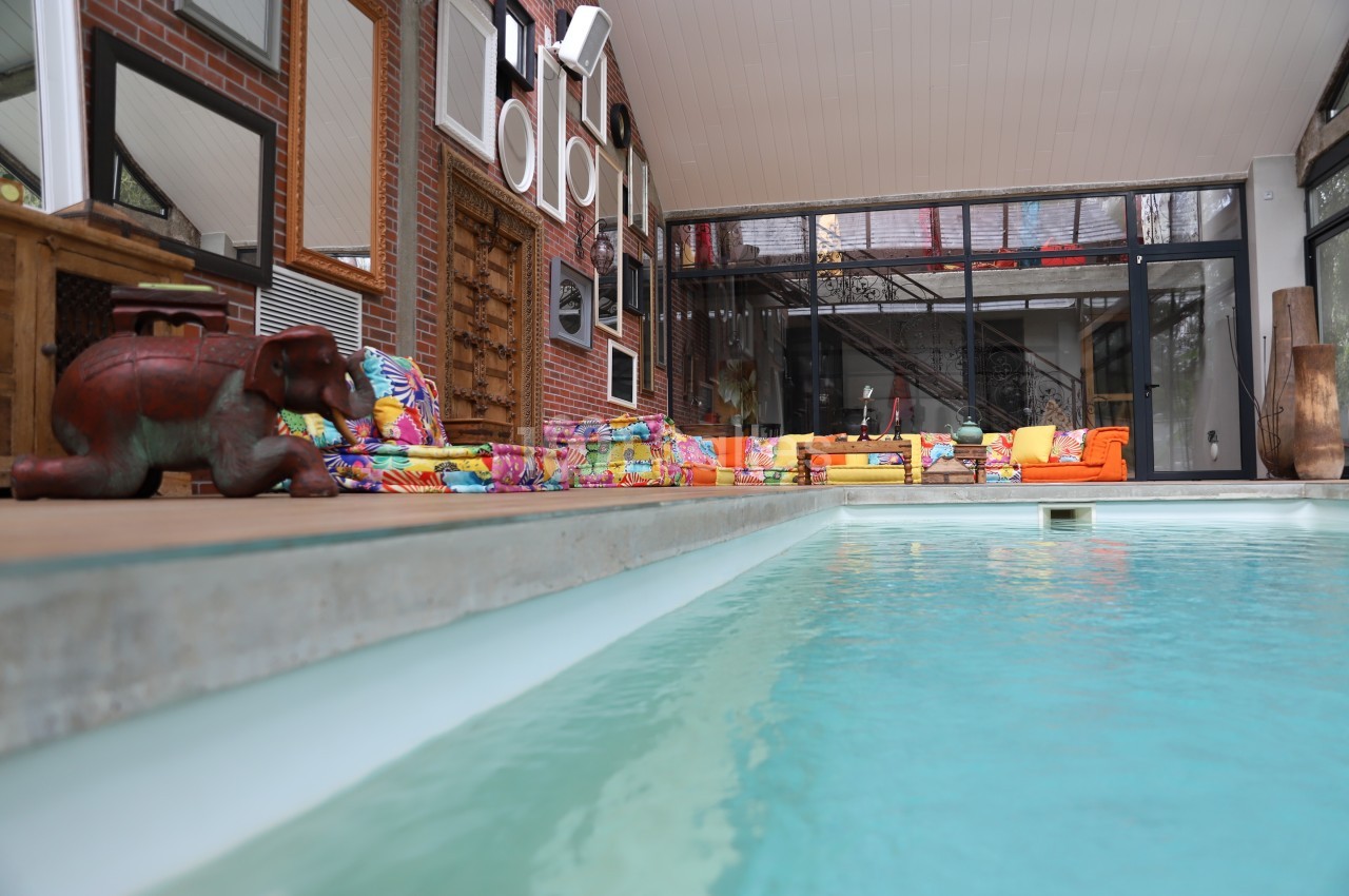 Piscine intérieure bordée de mobilier coloré et de décorations murales dans un espace lumineux avec baies vitrées.