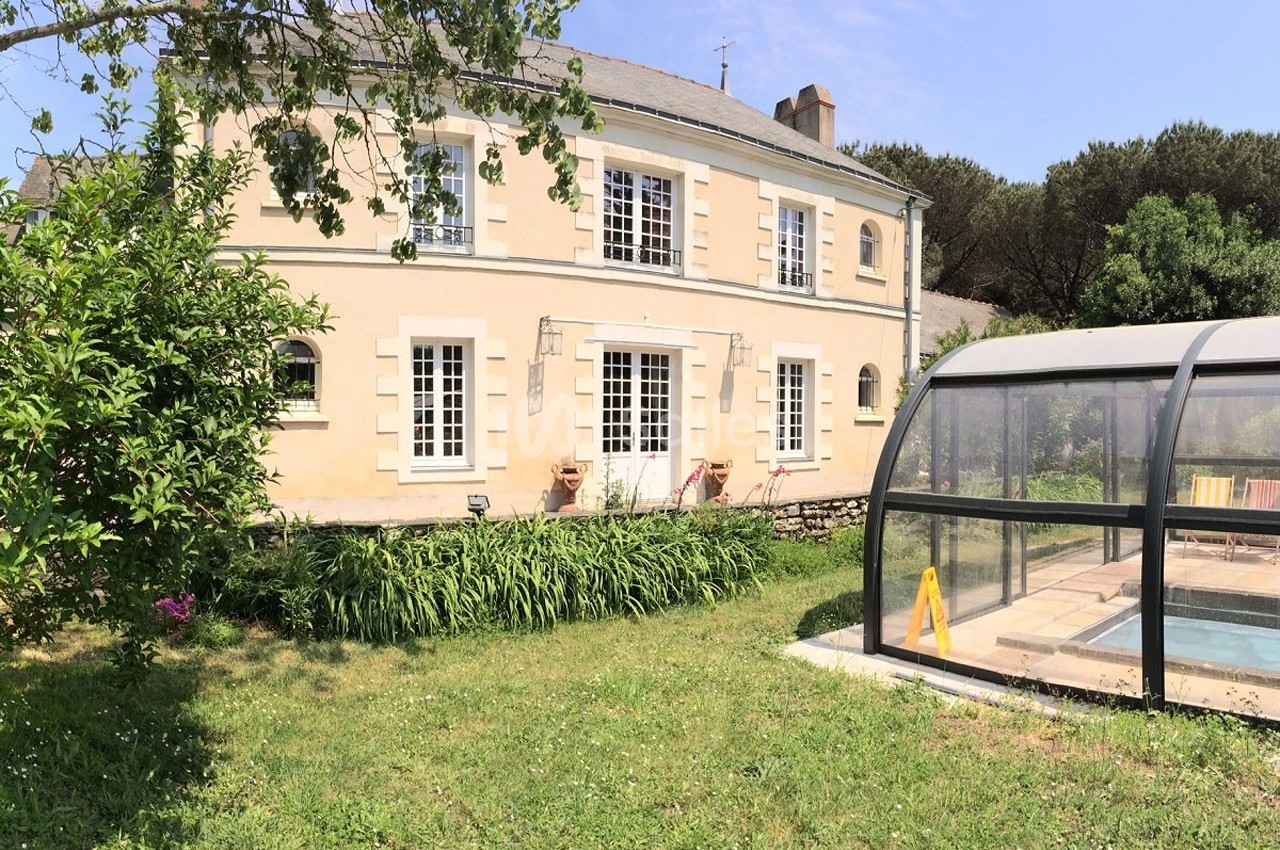 Maison en pierre avec jardin verdoyant et piscine couverte sous un ciel dégagé.
