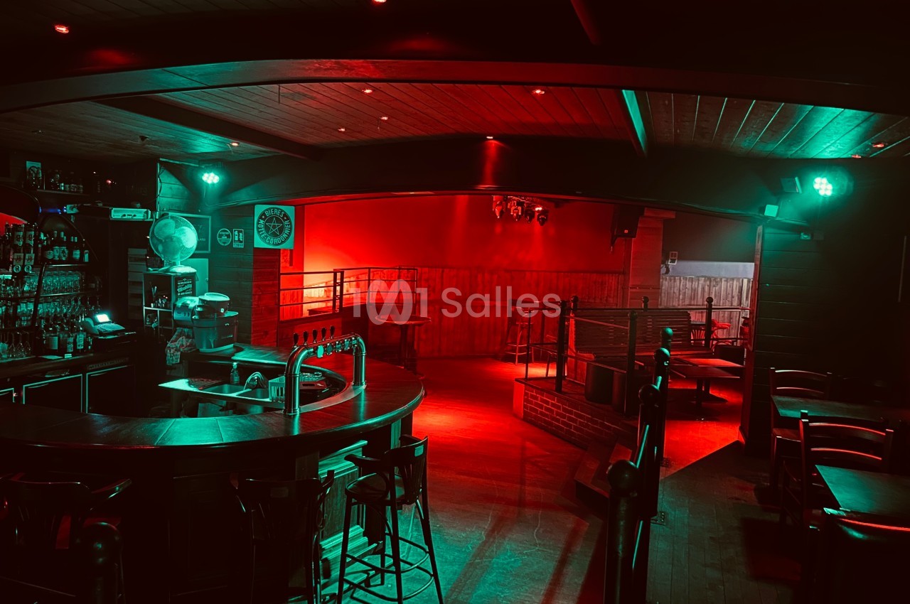Intérieur d'un bar vide avec éclairage rouge tamisé, comptoir central et tables en arrière-plan.