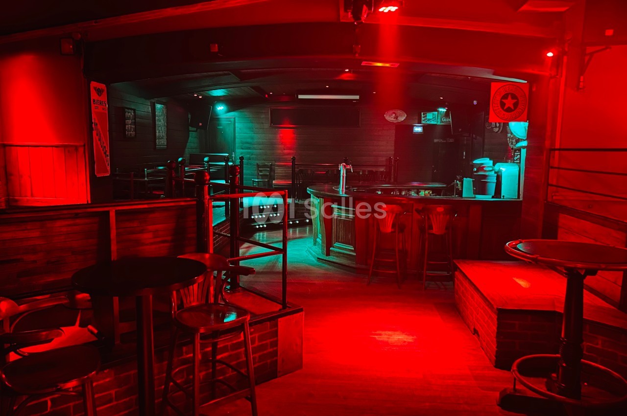 Salle de bar vide avec éclairage rouge et vert, comptoir en bois, tabourets hauts et ambiance tamisée.