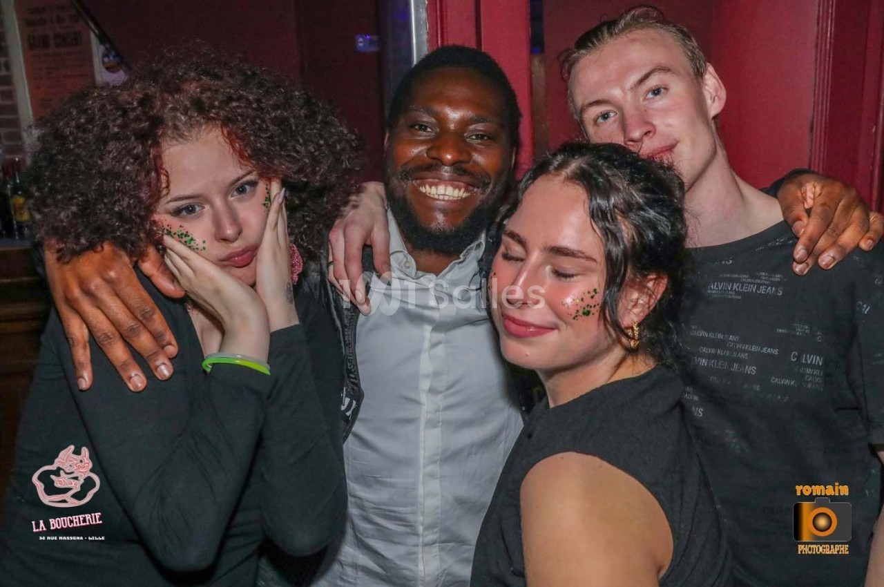 Quatre personnes souriantes posent ensemble dans un environnement festif, avec des décorations lumineuses sur leurs visages.