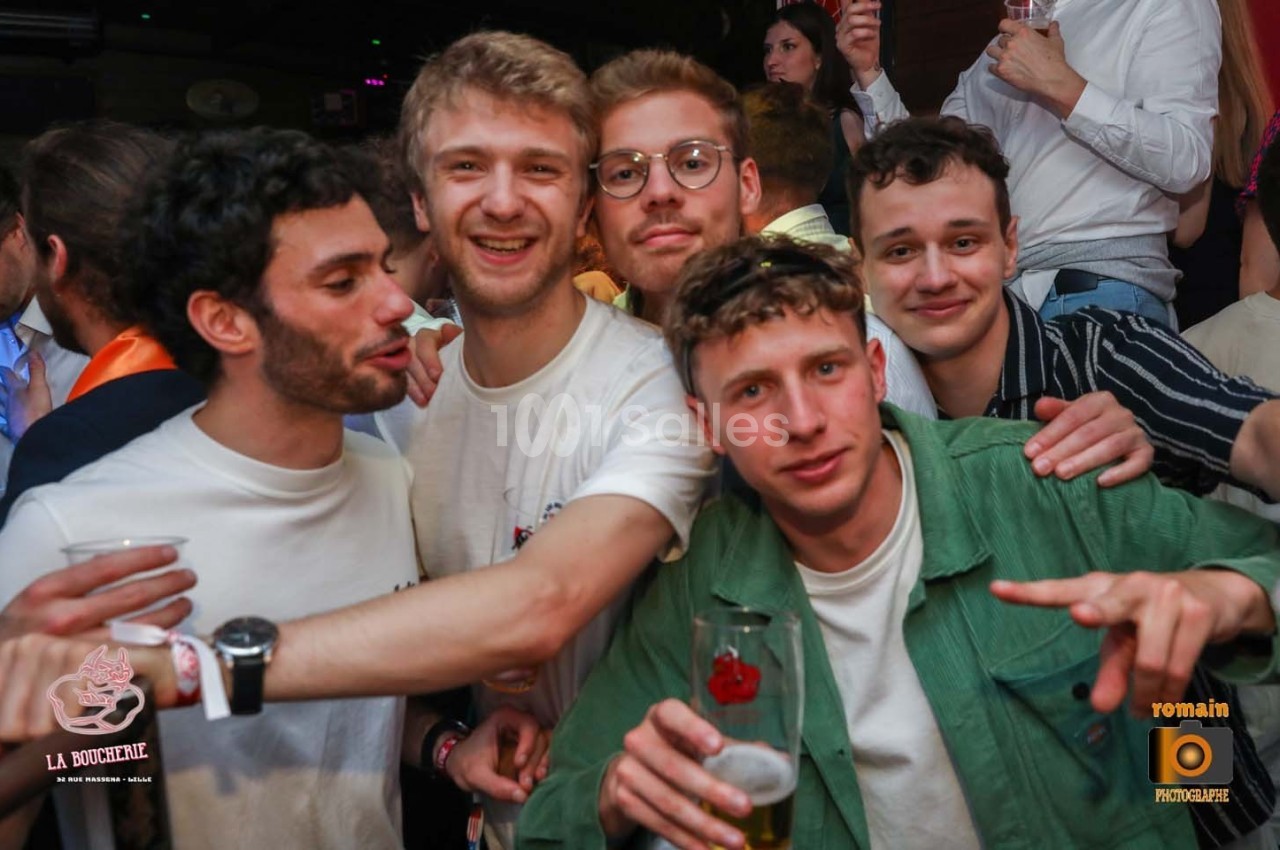 Cinq jeunes hommes souriants posent ensemble dans un environnement festif, certains tenant des verres à la main.