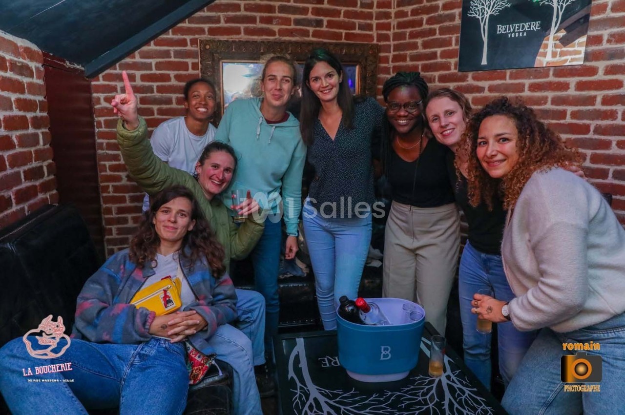 Un groupe de personnes souriantes posant dans un intérieur avec des murs en briques et un seau à boissons au centre.