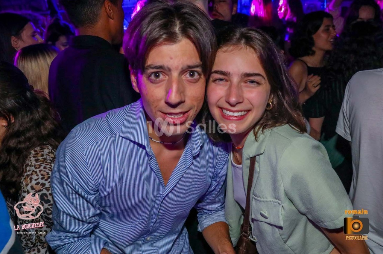 Un homme et une femme souriants posent ensemble dans une ambiance festive avec des lumières colorées en arrière-plan.
