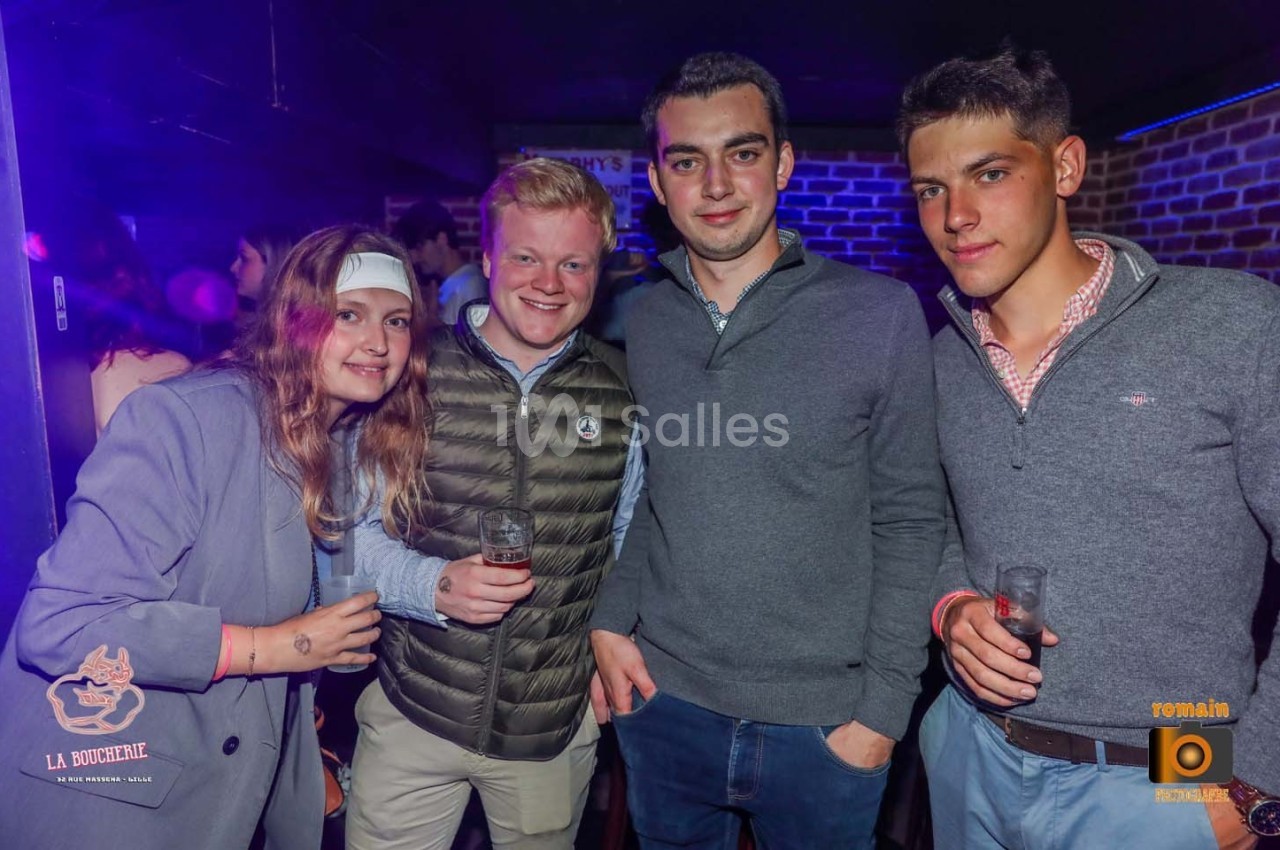 Quatre jeunes adultes posent ensemble dans un bar, tenant des verres, avec un éclairage tamisé et des logos visibles en…