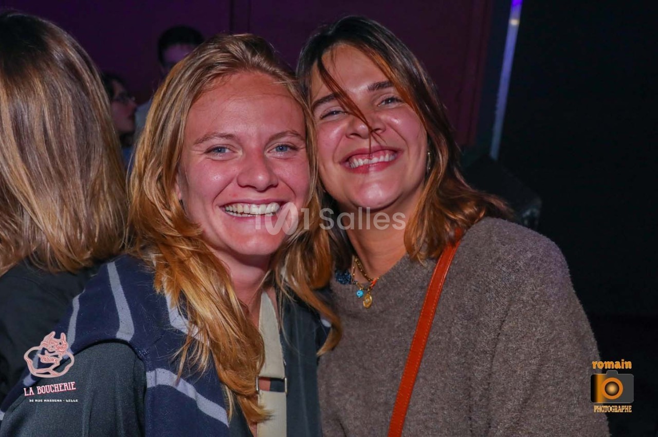 Deux femmes souriantes posent côte à côte dans un environnement intérieur sombre.