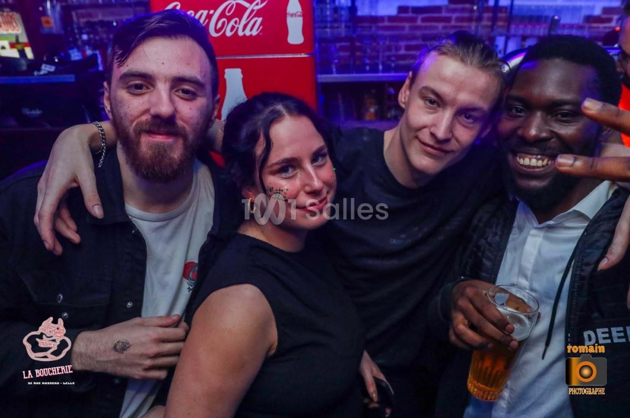 Quatre personnes souriantes posent dans un bar, avec des boissons et un décor lumineux en arrière-plan.