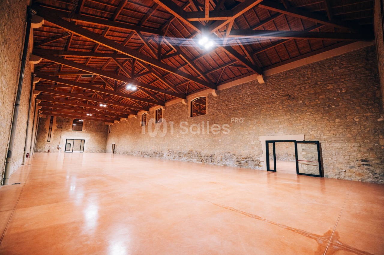 Intérieur d'une grande salle vide avec murs en pierre, plafond en bois et sol en béton poli.