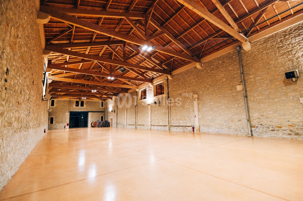Grande salle avec un sol en béton lisse, murs en pierre et plafond en bois avec poutres apparentes.