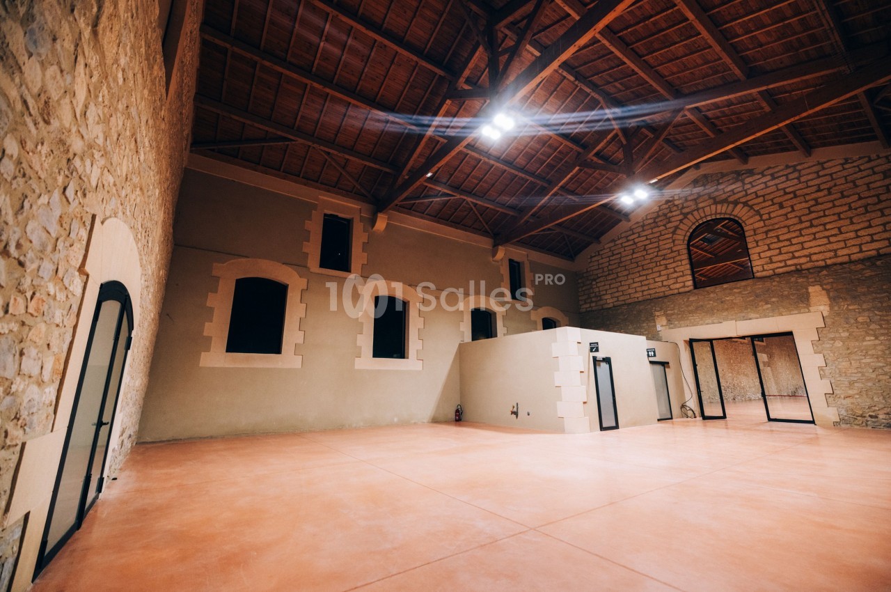 Intérieur d'une grande salle avec murs en pierre, plafond en bois et sol en béton lisse, éclairée par des lumières au…