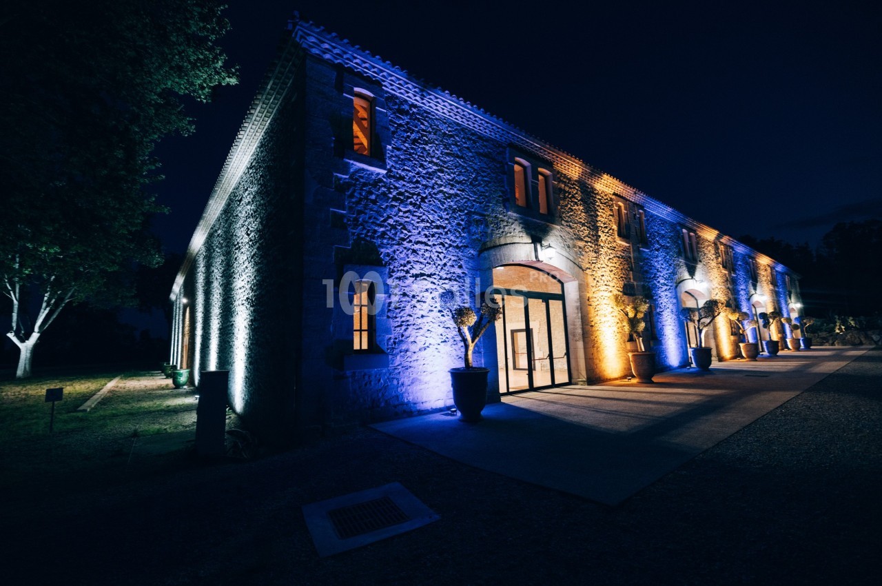 Façade d'un bâtiment en pierre éclairée par des lumières colorées bleues et jaunes, de nuit.