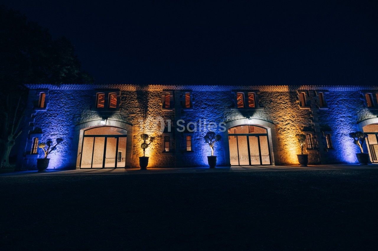 Façade d'un bâtiment en pierre éclairée par des lumières bleues et orange dans un environnement nocturne.