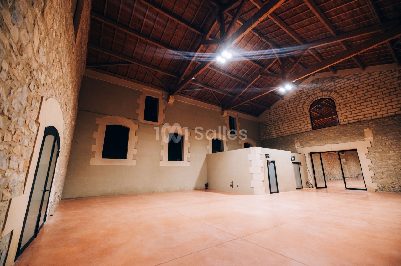 Intérieur d'une grande salle avec murs en pierre, plafond en bois et sol en béton lisse, éclairée par des lumières au…