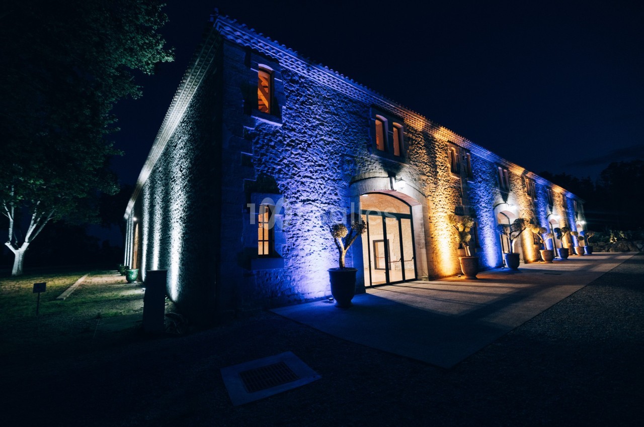 Façade d'un bâtiment en pierre éclairée par des lumières colorées bleues et jaunes, de nuit.