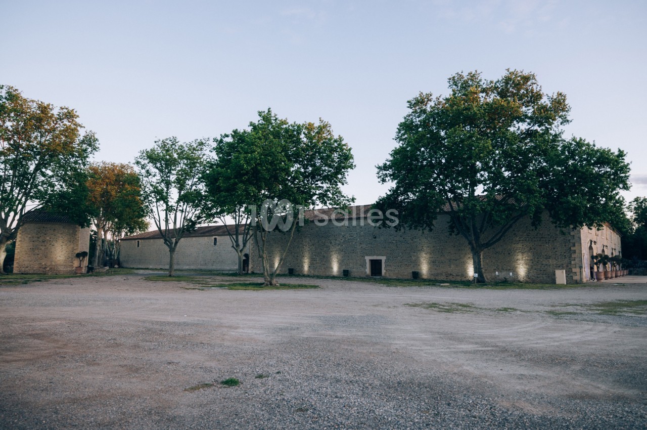 Bâtiment en pierre entouré d'arbres, avec un sol en gravier au premier plan et un éclairage discret sur les murs.