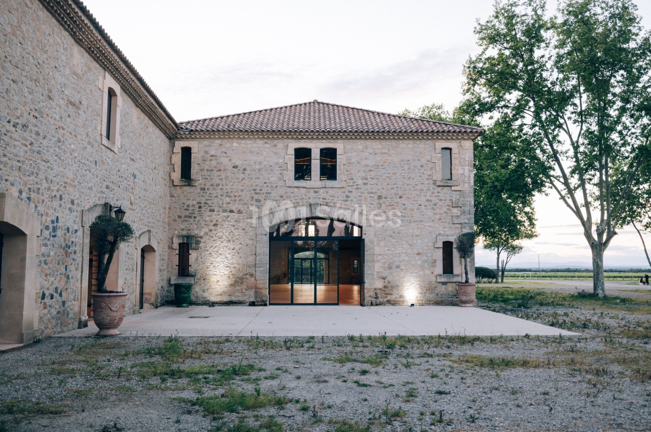 Bâtiment en pierre avec une grande porte vitrée, entouré d'arbres et situé dans un environnement rural.