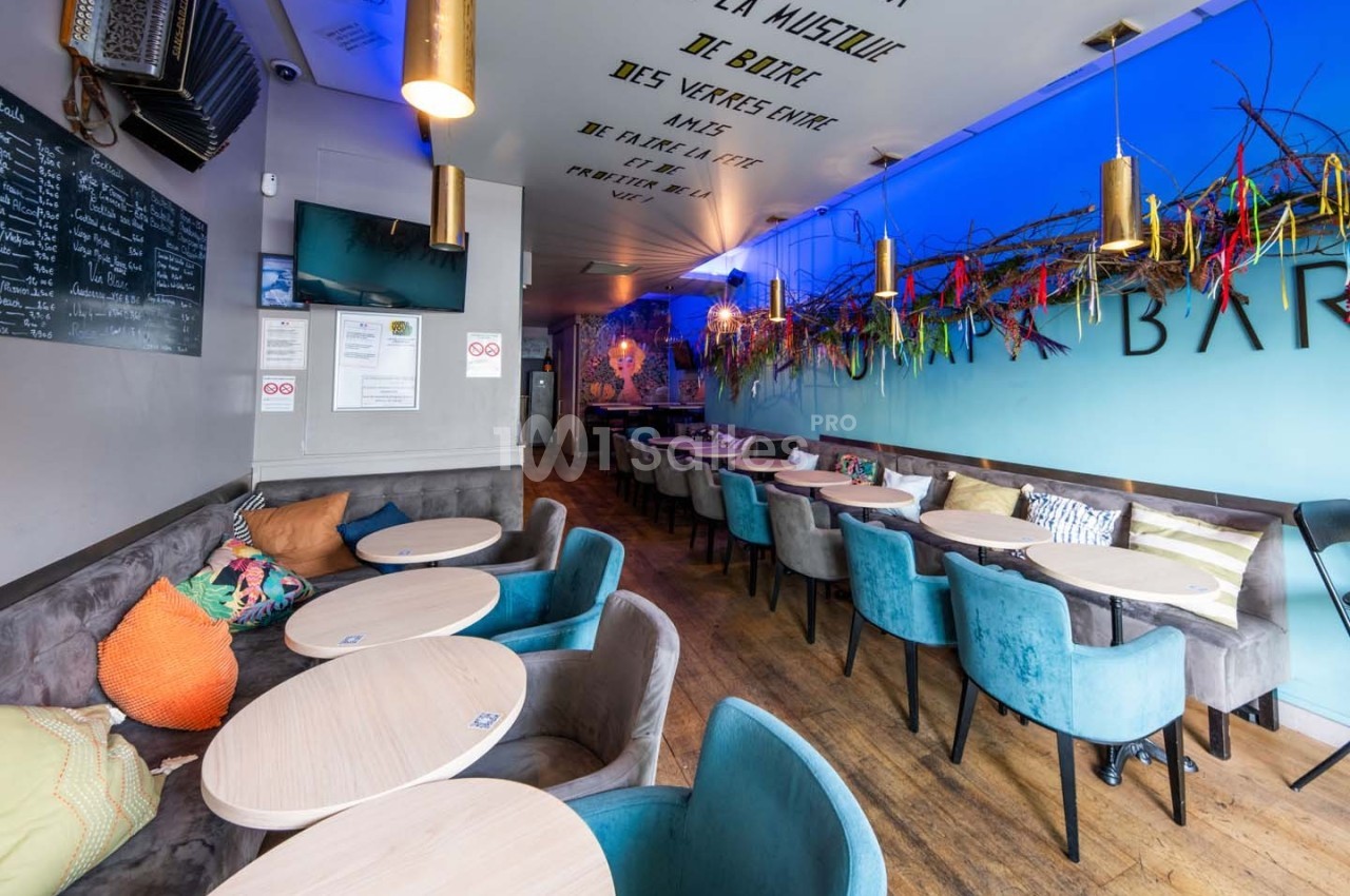 Salle de bar moderne avec tables rondes, chaises colorées, décorations murales et éclairage suspendu.