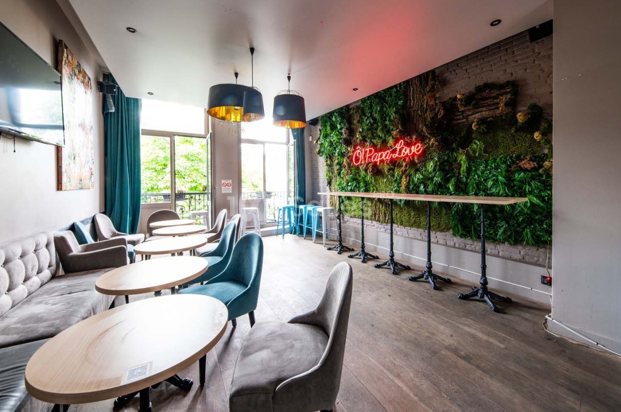 Salle lumineuse avec tables rondes, chaises modernes, mur végétal et enseigne néon rouge ’Pizza & Love’.