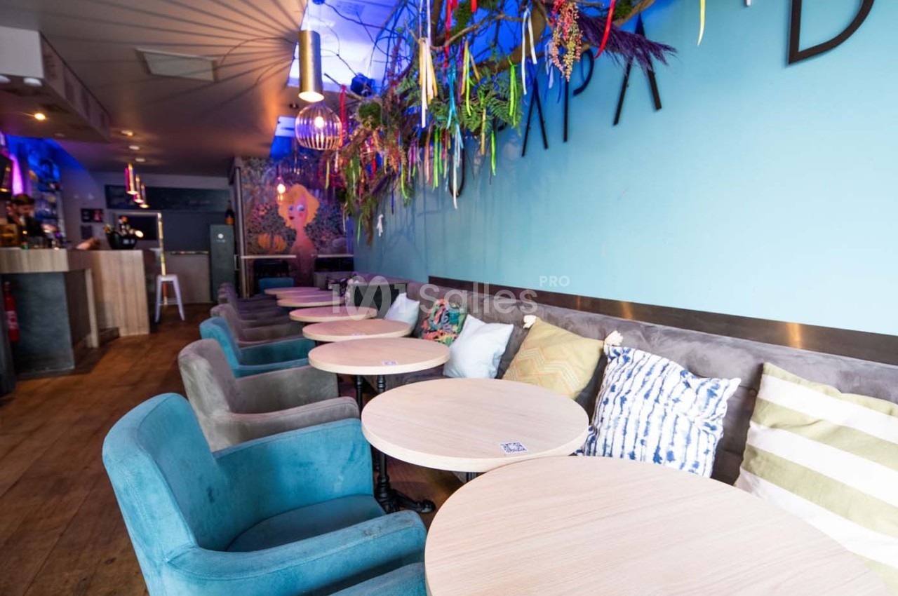 Salle de café moderne avec des tables rondes, des fauteuils colorés et une décoration murale végétale.