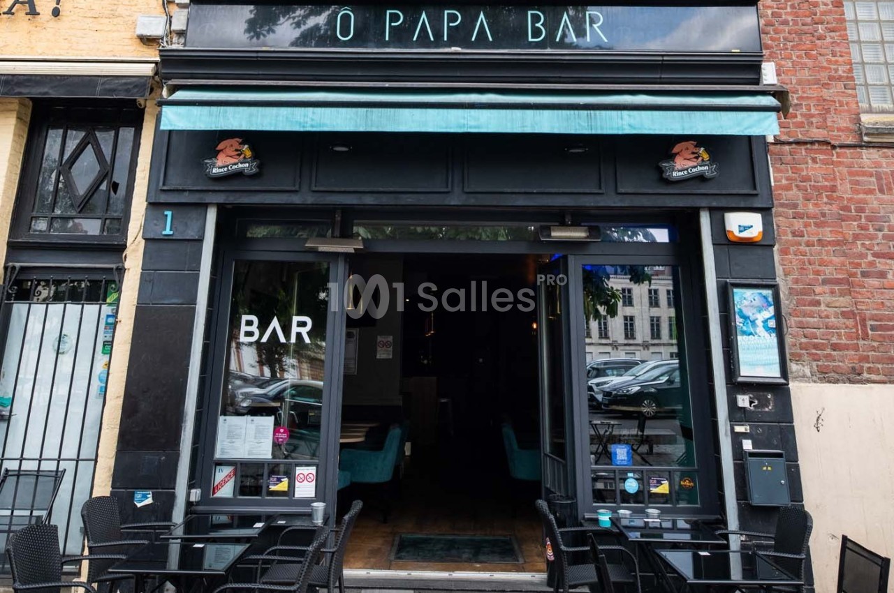 Façade d'un bar avec terrasse extérieure, enseigne lumineuse et porte ouverte donnant sur l'intérieur.