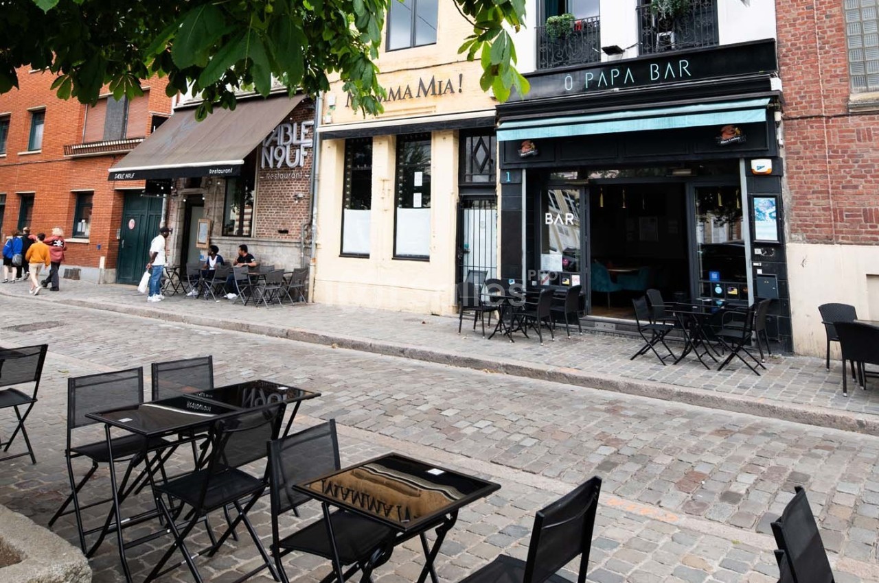 Terrasse vide de cafés et restaurants sur une rue pavée bordée de bâtiments en briques et en pierre.