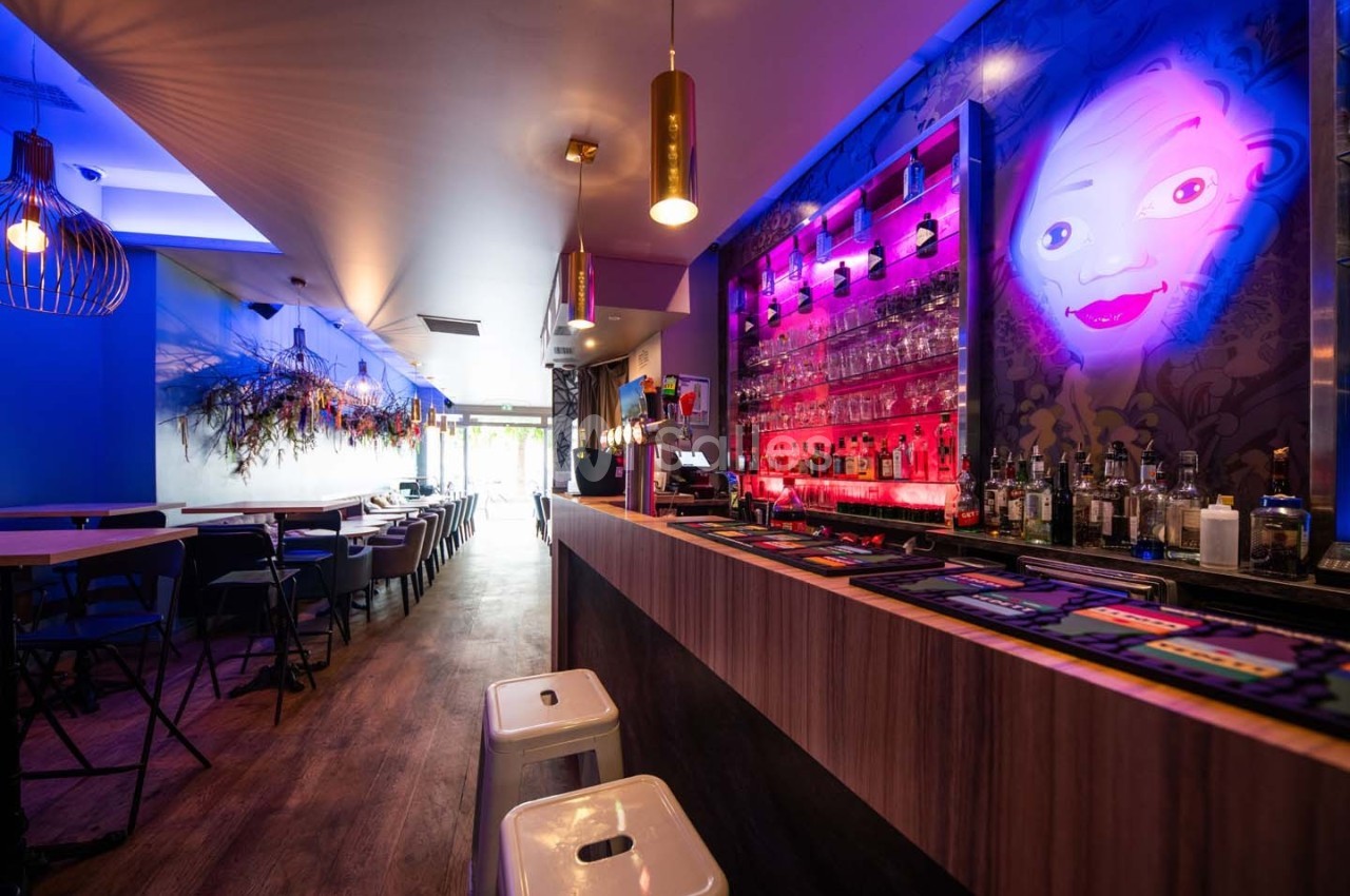 Intérieur d'un bar moderne avec un comptoir éclairé, des tabourets et une décoration murale colorée.