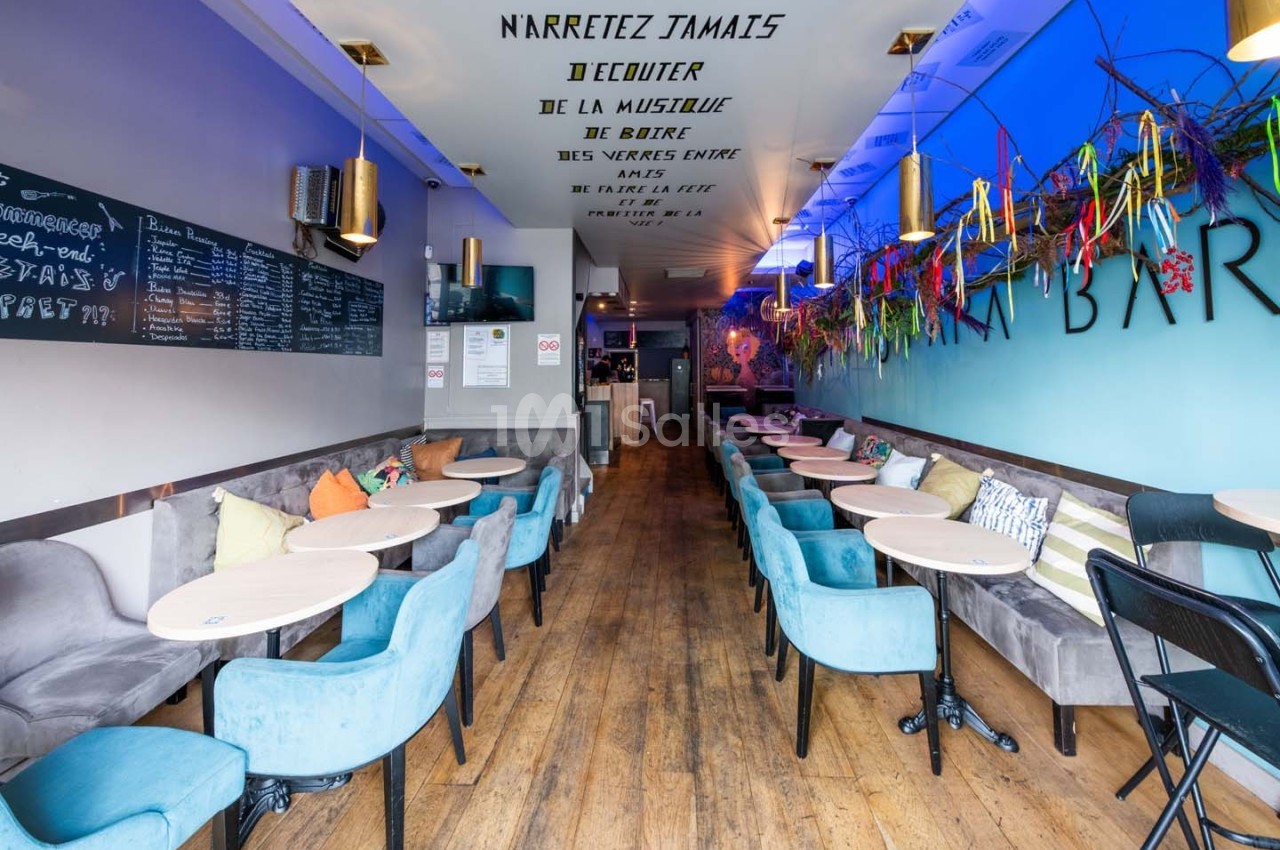 Intérieur d'un café moderne avec tables, chaises colorées et décoration murale artistique.