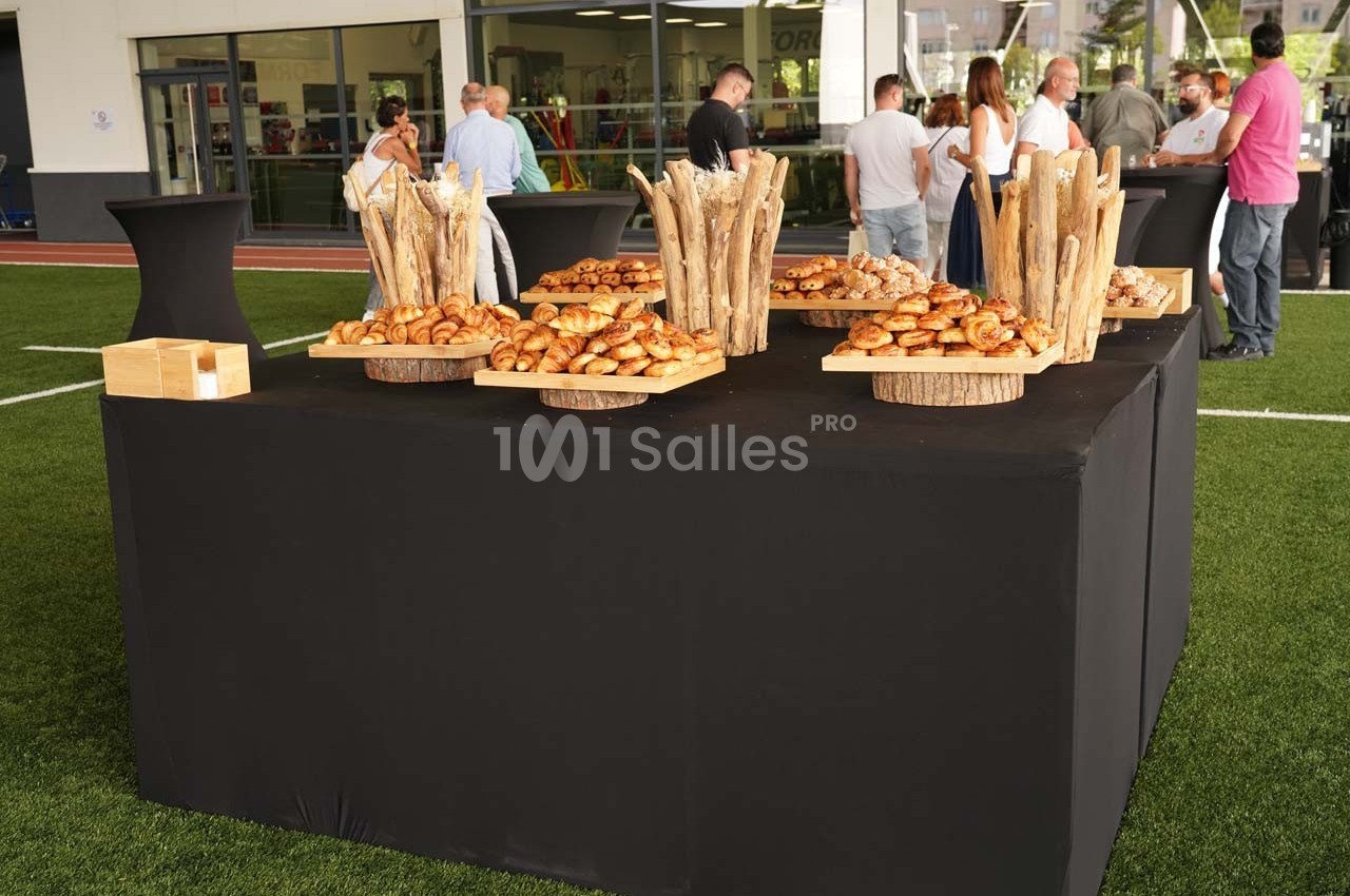 Table dressée avec des plateaux de viennoiseries et décorations en bois, entourée de personnes en arrière-plan.