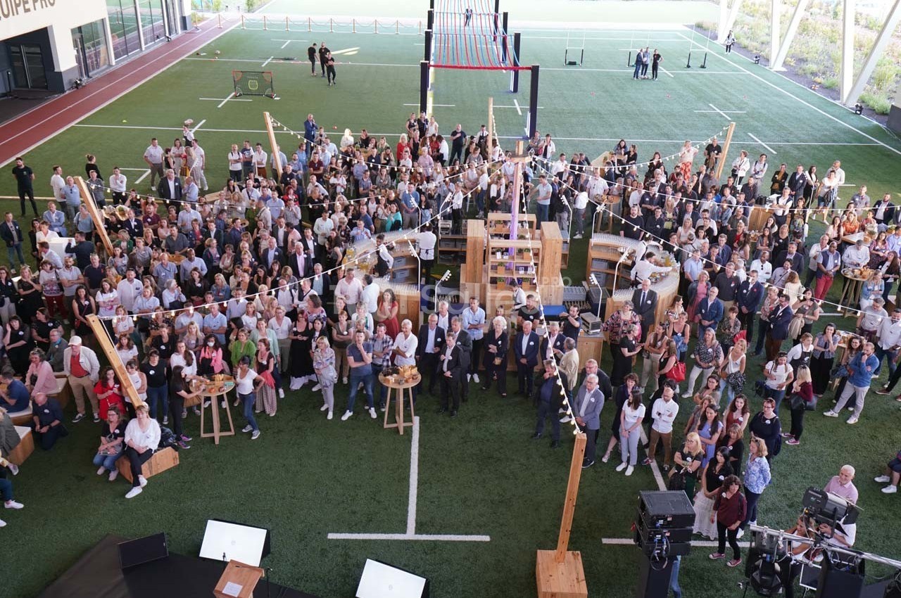 Vue aérienne d'un rassemblement de personnes dans un espace extérieur couvert, avec des tables hautes et une ambiance…