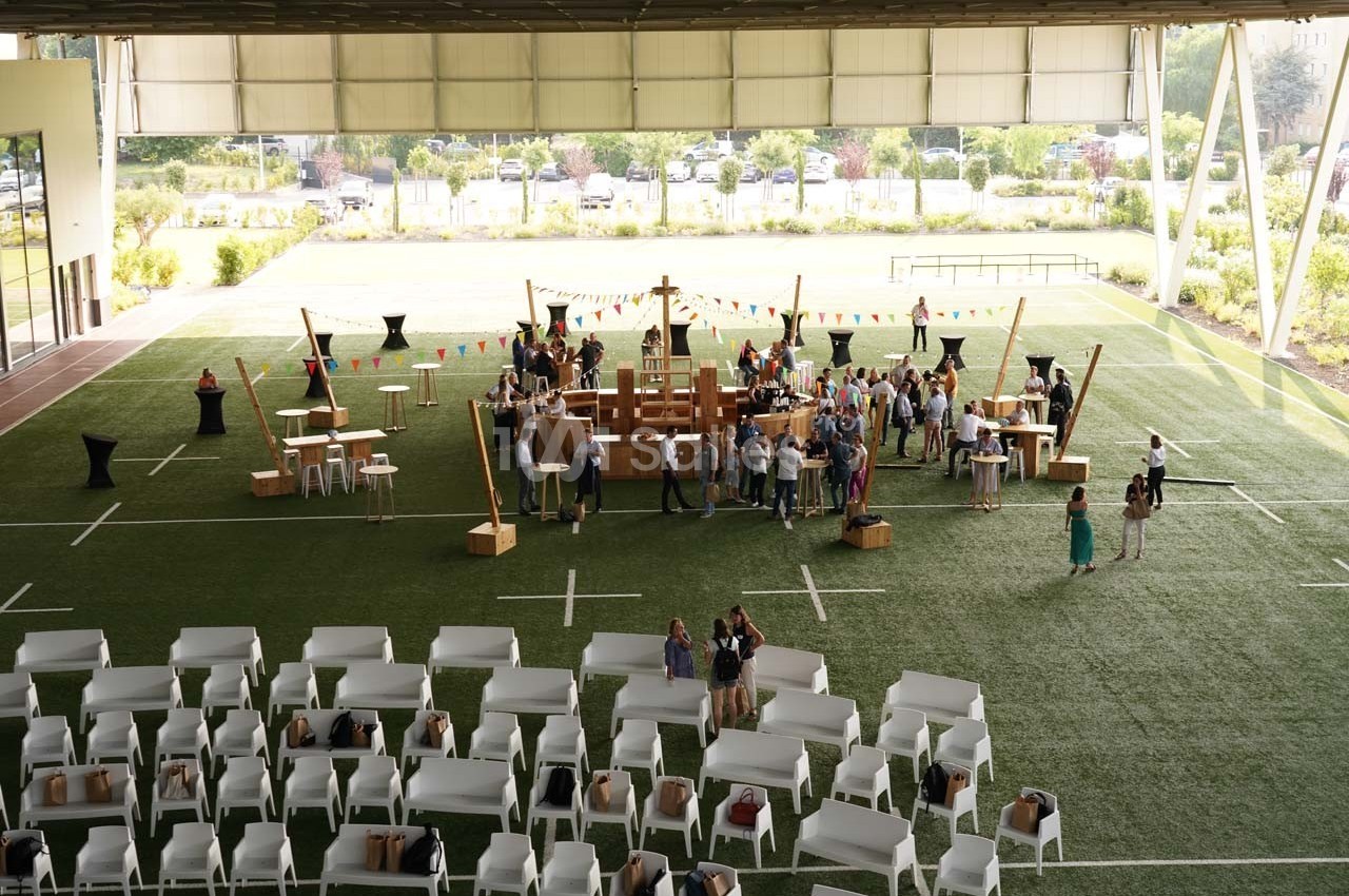 Des personnes participent à un événement sur un terrain couvert avec des stands, des décorations et des chaises disposées.
