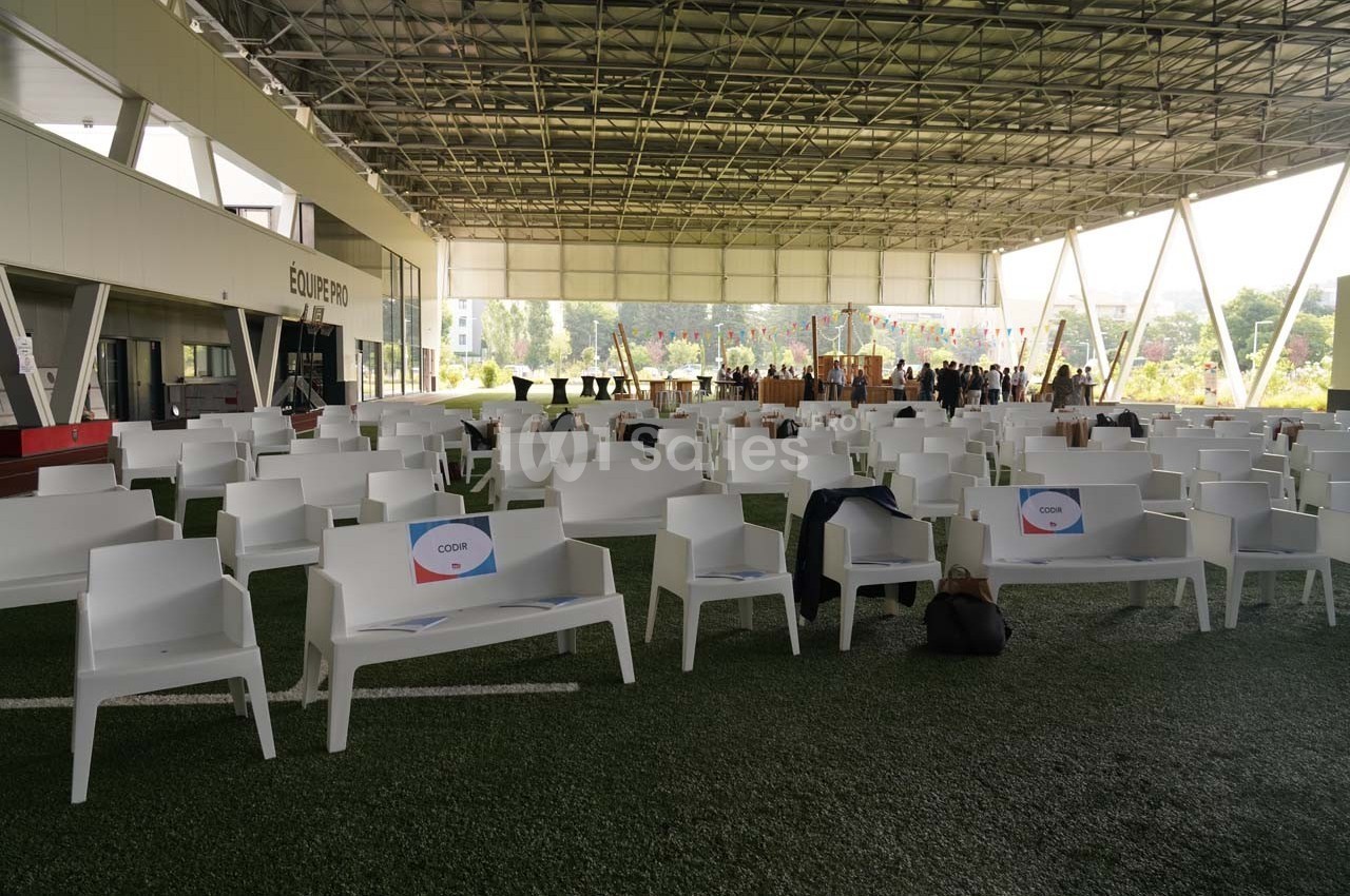 Chaises blanches alignées sous une structure couverte, avec des panneaux et une zone d'accueil en arrière-plan.